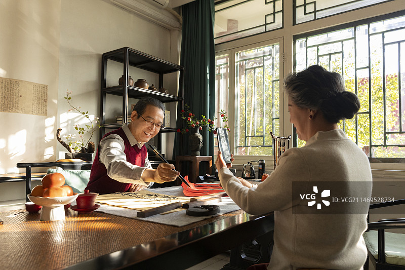 东方家庭过年：老年妻子在书房给正在写毛笔字的丈夫拍照、录视频图片素材