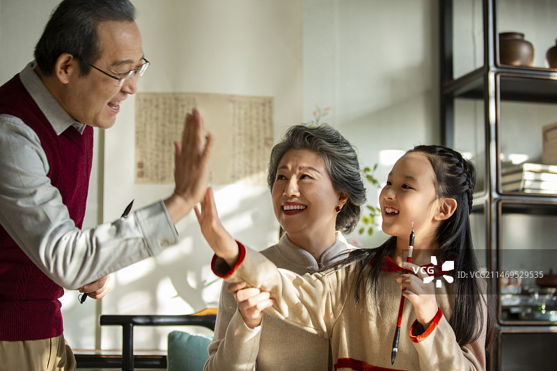 东方家庭过年：老年夫妇在书房教孙女写毛笔字，欢呼击掌图片素材