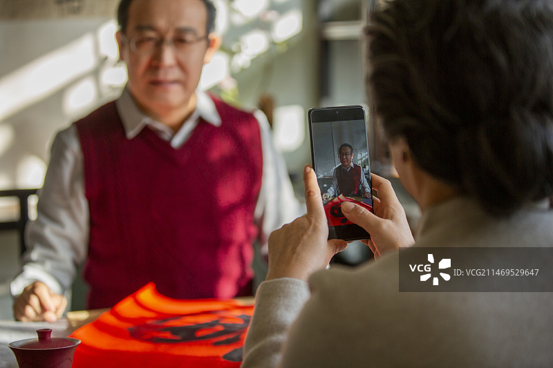 东方家庭过年：老年女子给在书房写福字的丈夫拍照图片素材