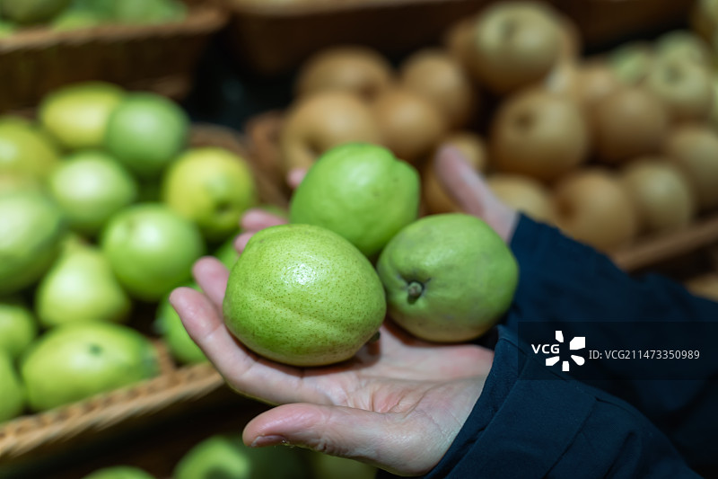 在超市果蔬区一个女孩手提购物蓝在过道上挑选新鲜的水果图片素材