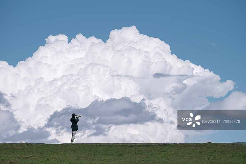 一团巨大的白色云朵下，一个行人站在草地上拍照图片素材