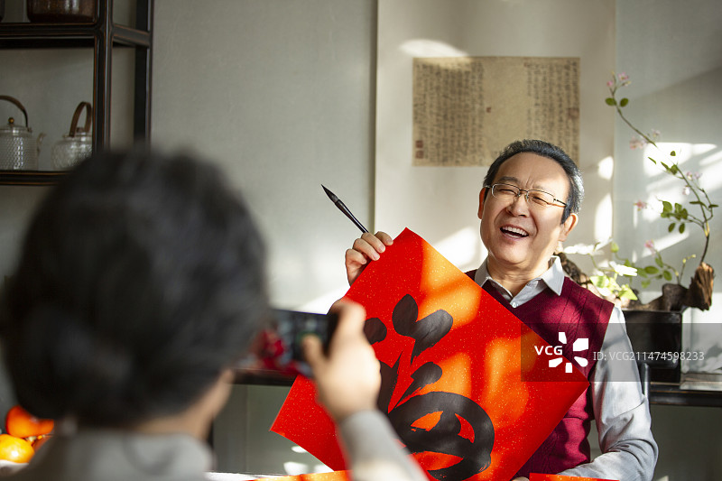 东方家庭过年：老年妻子在书房给拿着福字的丈夫拍照、录视频图片素材