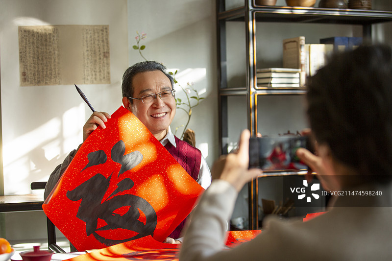 东方家庭过年：老年妻子在书房给拿着福字的丈夫拍照、录视频图片素材