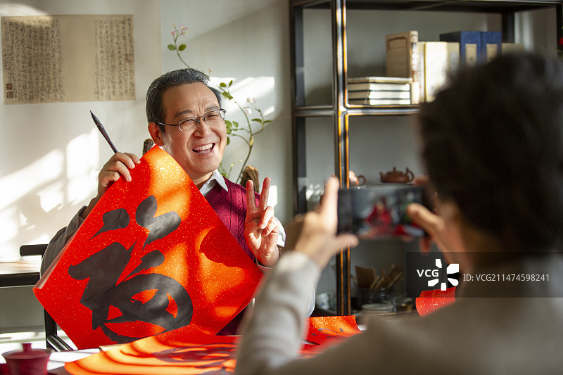 东方家庭过年：老年妻子在书房给拿着福字的丈夫拍照、录视频图片素材