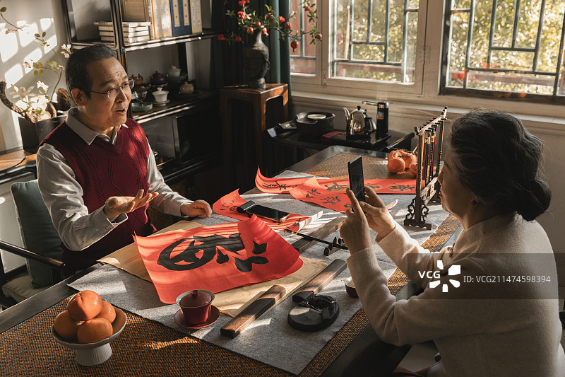 东方家庭过年：老年妻子在书房给写福字和春联的丈夫录视频图片素材