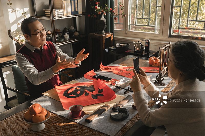 东方家庭过年：老年妻子在书房给写福字和春联的丈夫录视频图片素材