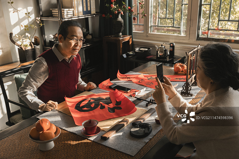 东方家庭过年：老年妻子在书房给写福字和春联的丈夫拍照、录视频图片素材