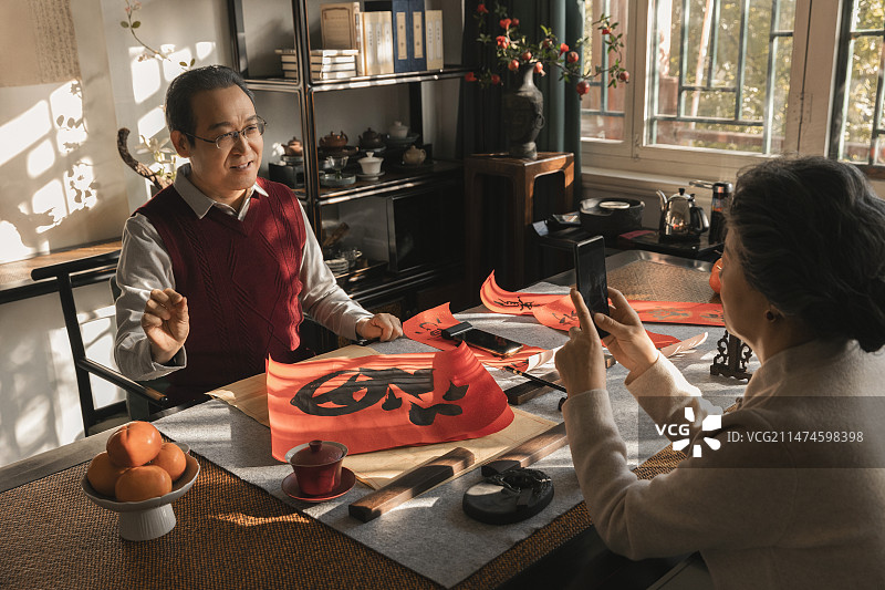 东方家庭过年：老年妻子在书房给写福字和春联的丈夫拍照、录视频图片素材