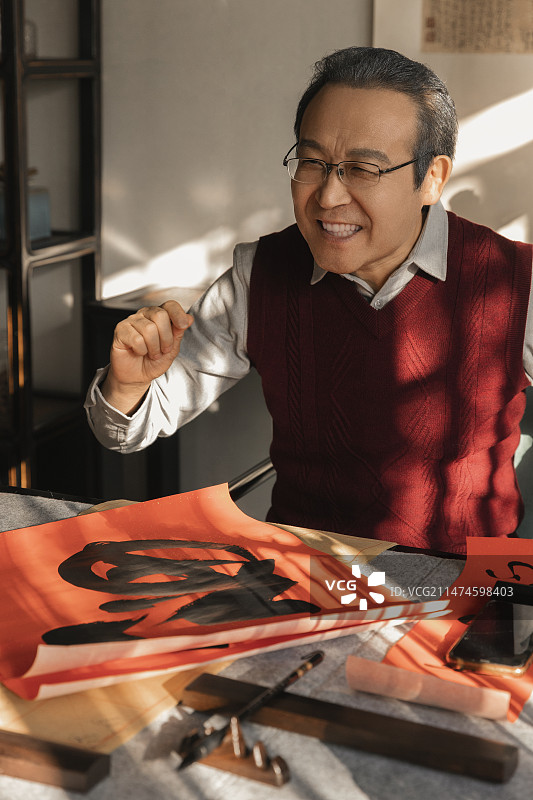 东方家庭过年：老年男子在书房给写福字和春联图片素材