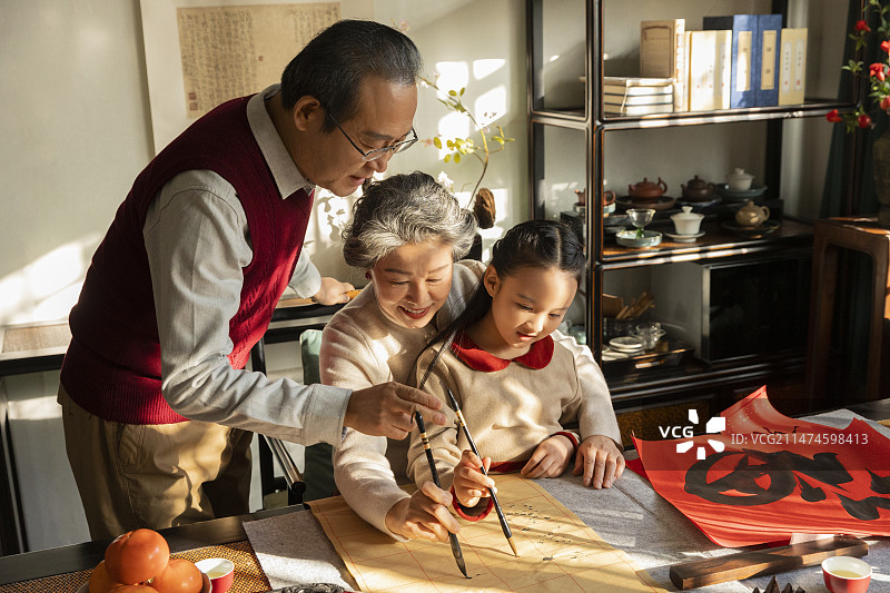 东方家庭过年：老年夫妇在书房教孙女写毛笔字图片素材