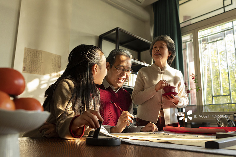 东方家庭过年：老年夫妇和孙女在书房写毛笔字、喝茶、聊天嬉戏图片素材