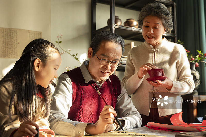 东方家庭过年：老年夫妇和孙女在书房写毛笔字、喝茶、聊天嬉戏图片素材