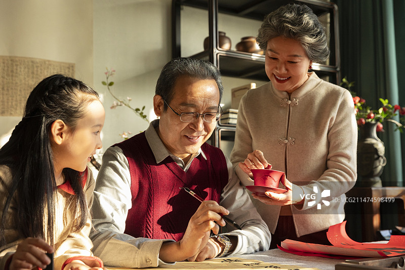 东方家庭过年：老年夫妇和孙女在书房写毛笔字、喝茶、聊天嬉戏图片素材