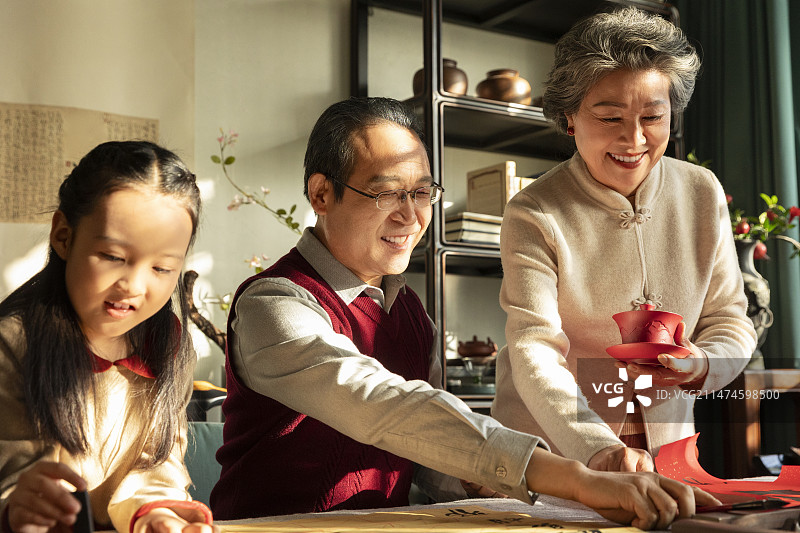 东方家庭过年：老年夫妇和孙女在书房写毛笔字、喝茶、聊天嬉戏图片素材