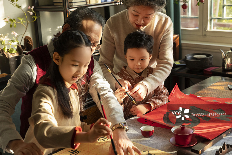 东方家庭过年：老年夫妇在书房教孙女和孙子写毛笔字图片素材