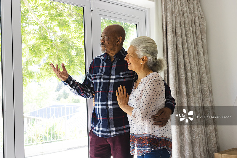拥抱、交谈并眺望阳光明媚的家的老年夫妇图片素材