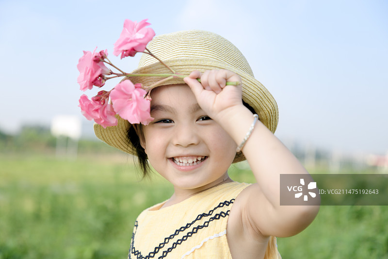 手拿小红花带着帽子对着镜头笑的小女孩正脸图片素材