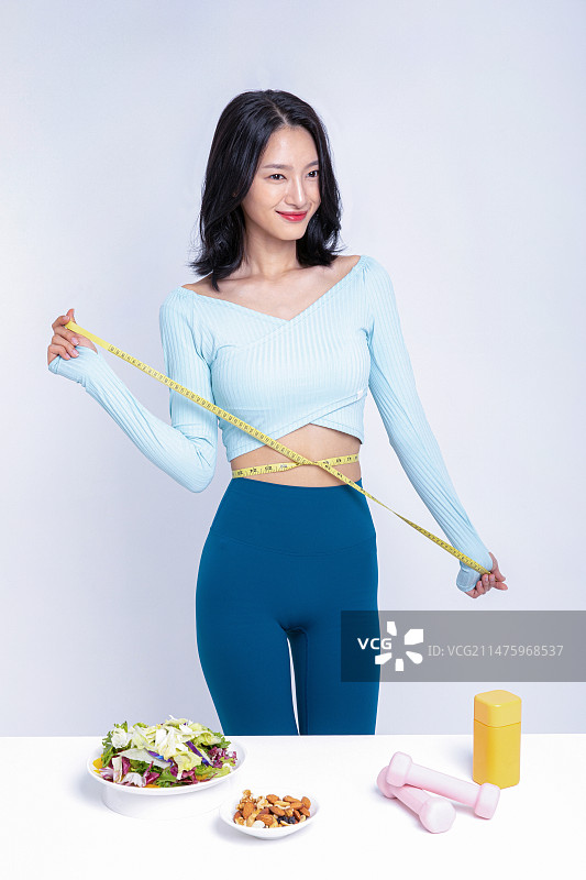 在沙拉坚果舌下胶带测量丸盒前用卷尺测量腰围的女人图片素材