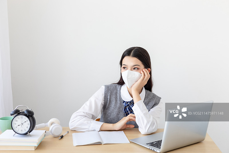 室内一个戴着KN95口罩的中国女大学生在学习图片素材