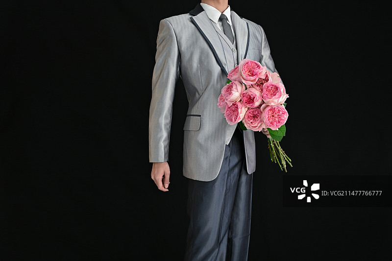 黑色背景下拿着花束的男人的中间部分图片素材