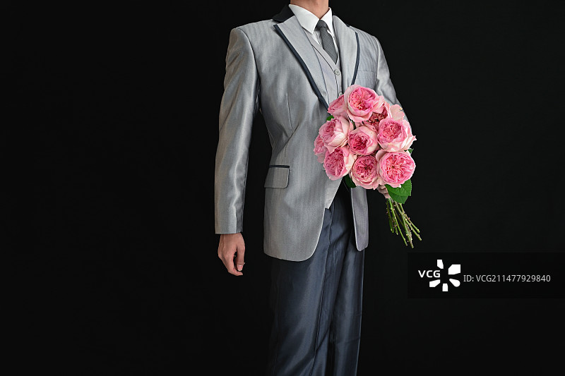 黑色背景下拿着花束的男人的中间部分图片素材