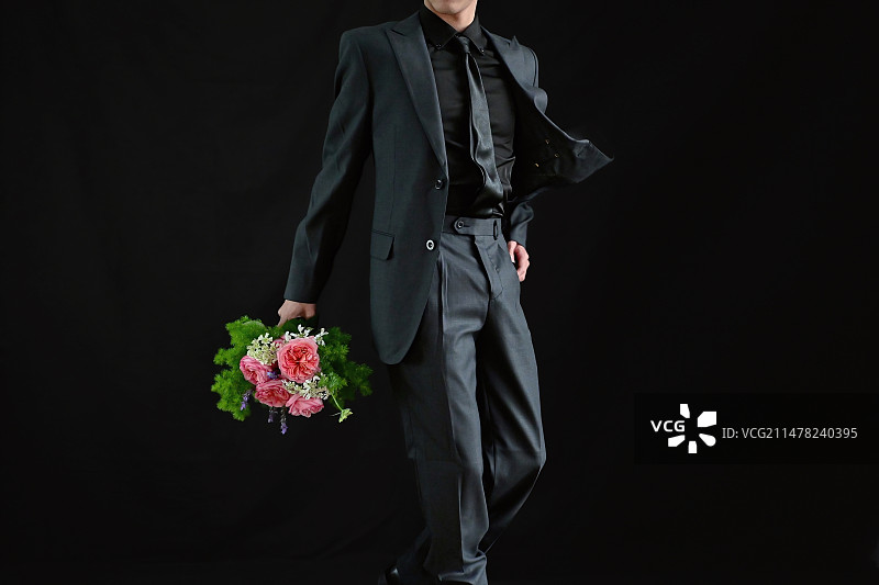 黑色背景下拿着花束的男人的中间部分图片素材