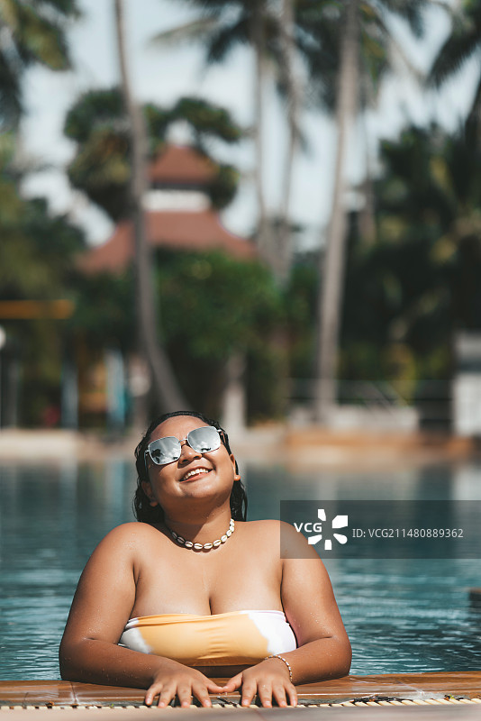 女子坐在泳池边，手持充气甜甜圈图片素材