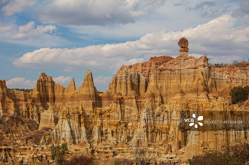 蓝天白云下云南元谋浪巴铺土林，沙砾岩壁褶皱起伏万壑丛生，锥柱耸立，山顶巨石像橘子洲头主席雕塑图片素材