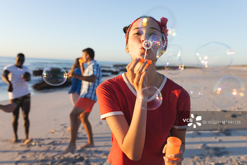 在阳光明媚的海滩上吹泡泡的年轻白人女性图片素材
