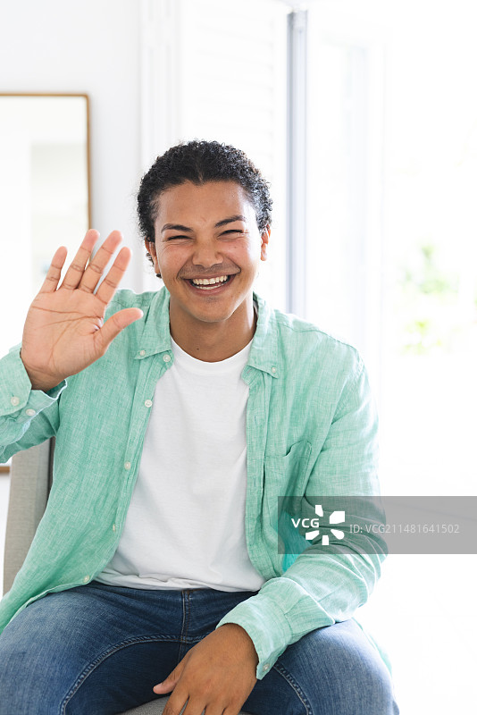 在明亮的家庭环境中进行视频通话时欢快挥手的年轻混血男子图片素材