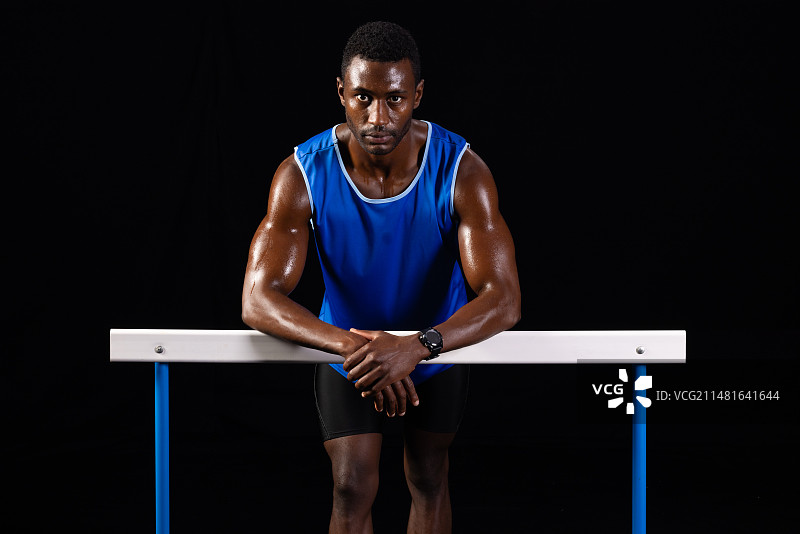 在黑色背景的跨栏上休息的非洲裔运动员（含留白）图片素材