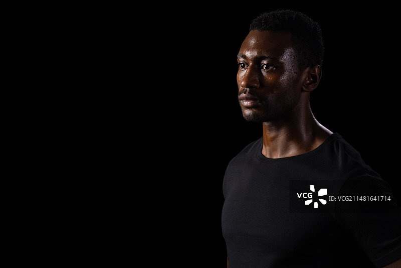 穿着黑色衬衫的非裔美国男人在黑色背景上沉思图片素材
