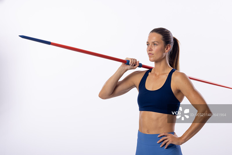 年轻的白人女运动员肩上扛着标枪，白色背景留有文案空间图片素材