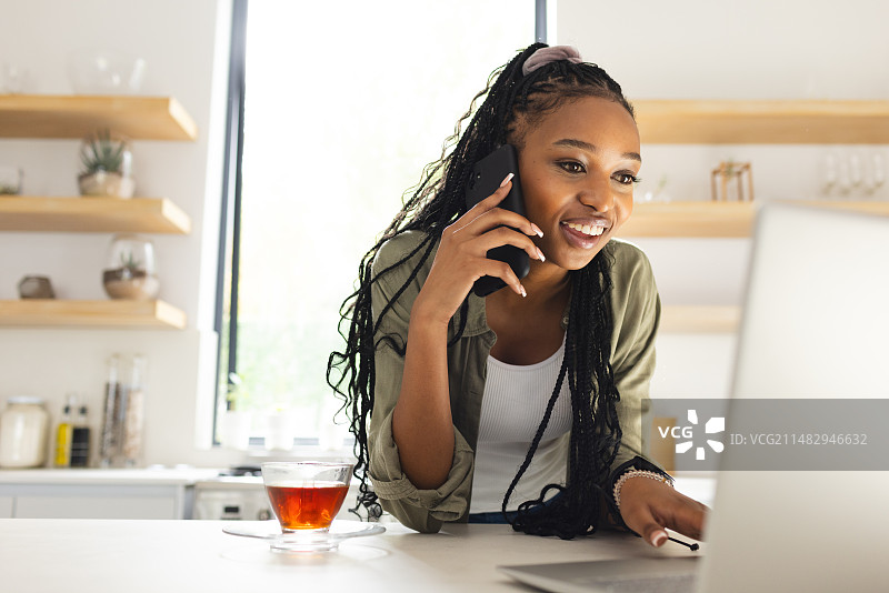 使用笔记本电脑时打电话的年轻非洲裔美国女性图片素材