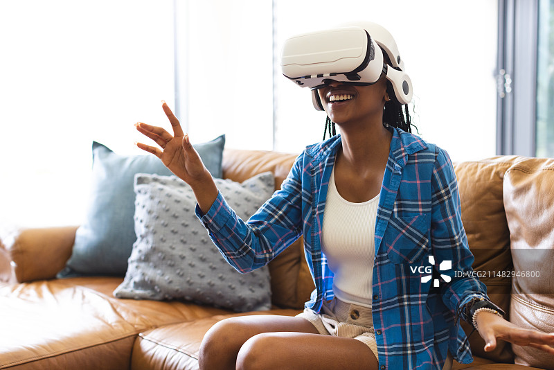 年轻非洲裔女人坐棕色皮沙发体验VR头显图片素材