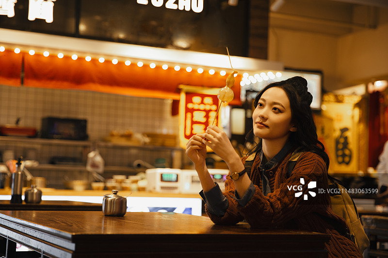 青年女子拿着葫芦糖人在城市美食街旅行图片素材