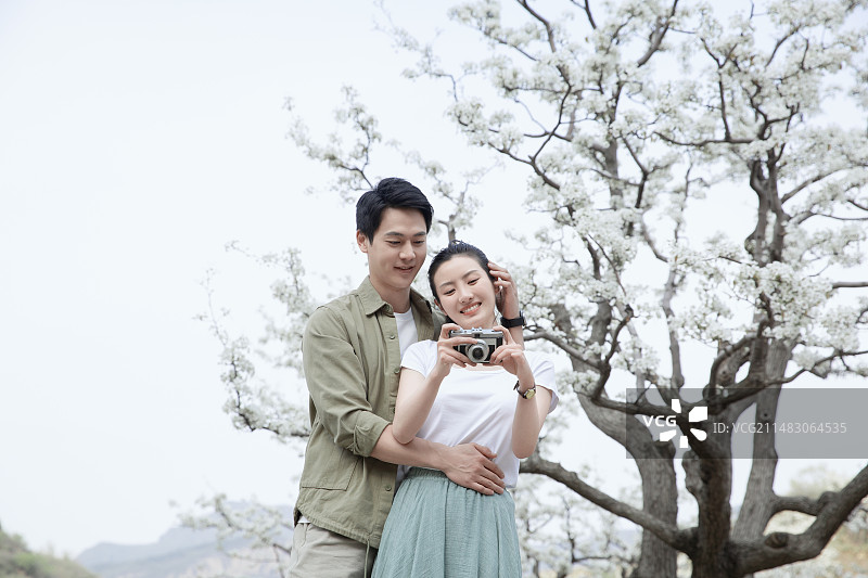 甜蜜情侣在户外旅行拿着相机看照片图片素材