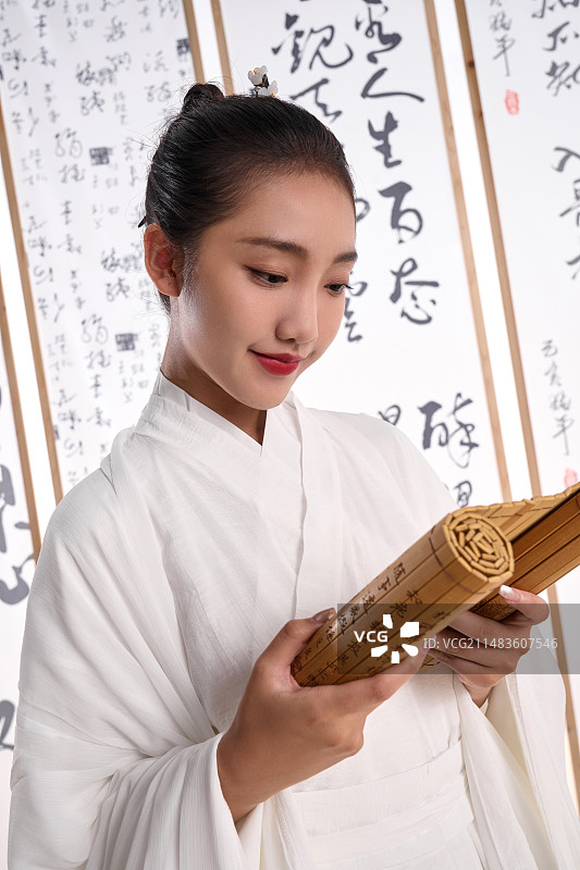 一位中国古装美女拿着竹简站在书法作品前图片素材