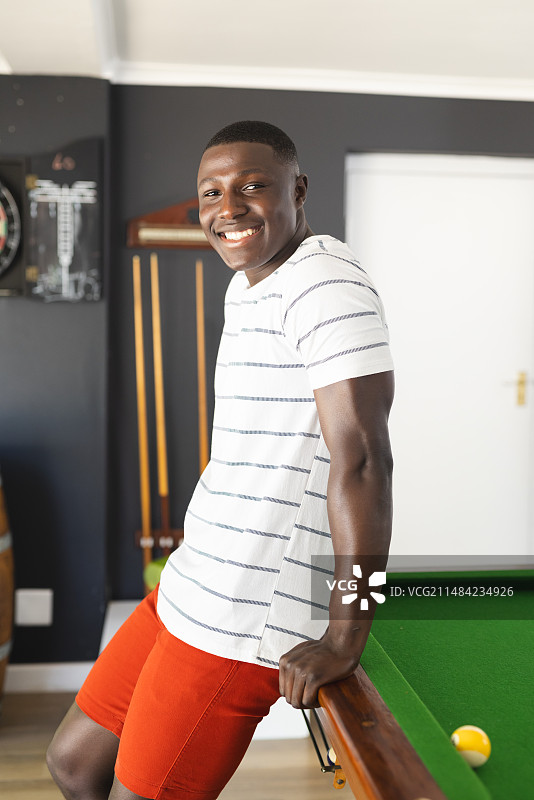 一位年轻的非裔美国男子靠在台球桌上，对着镜头微笑图片素材