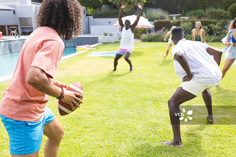 在后院派对上准备扔橄榄球的年轻非裔美国男人图片素材