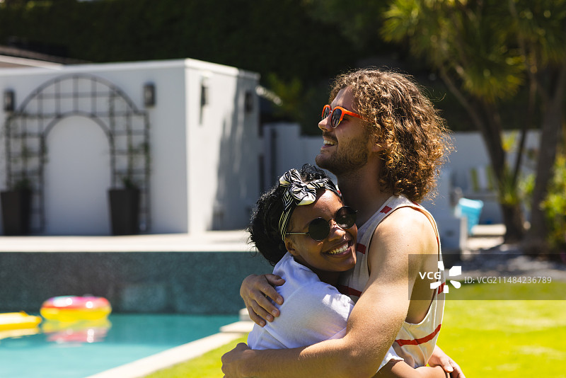年轻的非裔美国女人和白人男子在泳池旁拥抱图片素材
