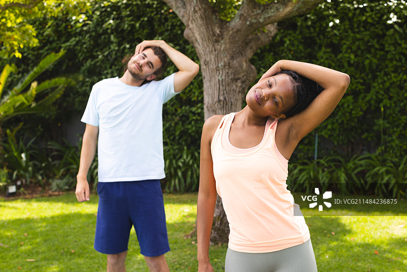 年轻白人男子和非裔美国女子在阳光明媚的后院伸展身体图片素材