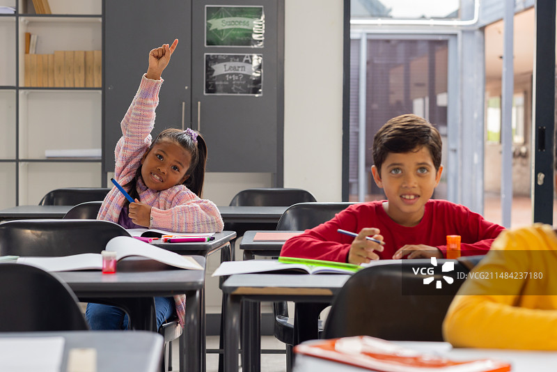 在学校教室里，穿着粉色格子衬衫的混血女孩积极举手图片素材