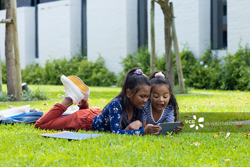 两个混血女孩躺在学校的草地上玩智能手机图片素材