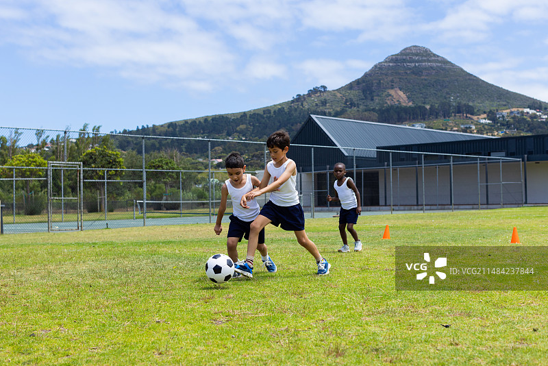 混血和非裔美国儿童在学校的草地上踢足球图片素材