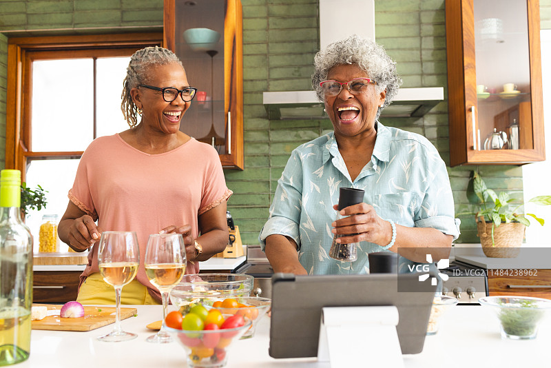 非裔美国老年妇女和混血老年妇女在厨房里分享欢乐时光图片素材