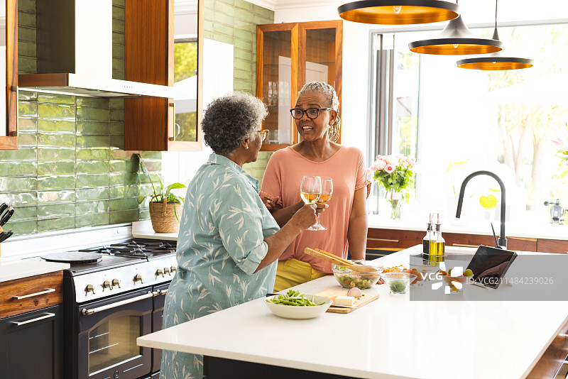 年长的非裔美国妇女和混血妇女在阳光明媚的厨房里敬酒图片素材