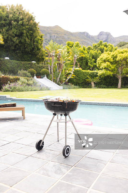 准备好的炭火烤架和美食，泳池边的葱郁花园图片素材
