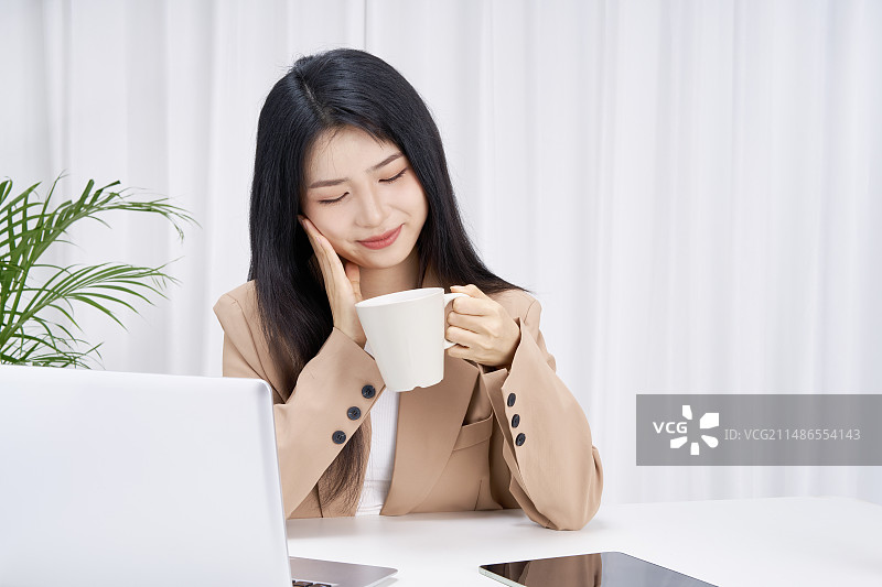 坐在办公桌前手拿水杯的年轻女孩图片素材