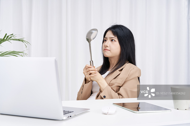 手拿勺子坐在办公桌前的年轻商务女孩图片素材